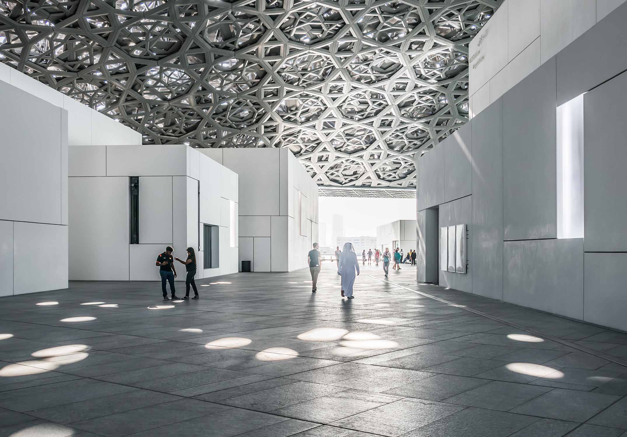 Innenhof im Kunstmuseum Louvre von Jean Nouvel in Abu-Dhabi. Weisse Baukörper mit riesigem Kuppeldach, das Lichtstrahlen, wie einen Lichtregen durchlässt.