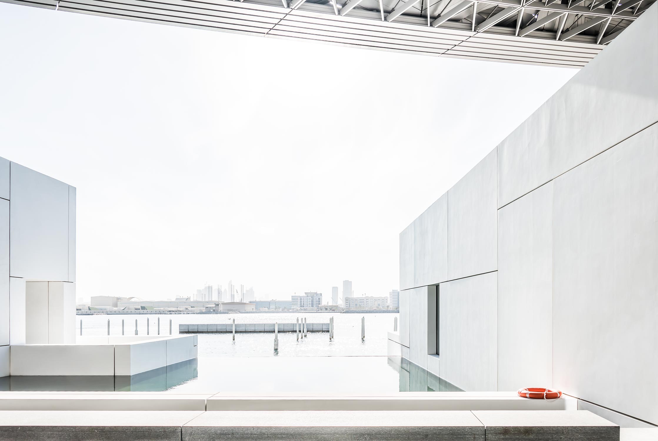 Aussicht vom Kunstmuseum Louvre von Jean Nouvel in Abu-Dhabi. Weisse Baukörper mit riesigem Kuppeldach, umgeben von türkisfarbenem Meerwasser.